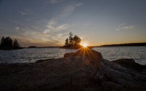 Sun setting behind a small island. There are some rocks in the foreground. Sun setting behind a small island. There are some rocks in the foreground.